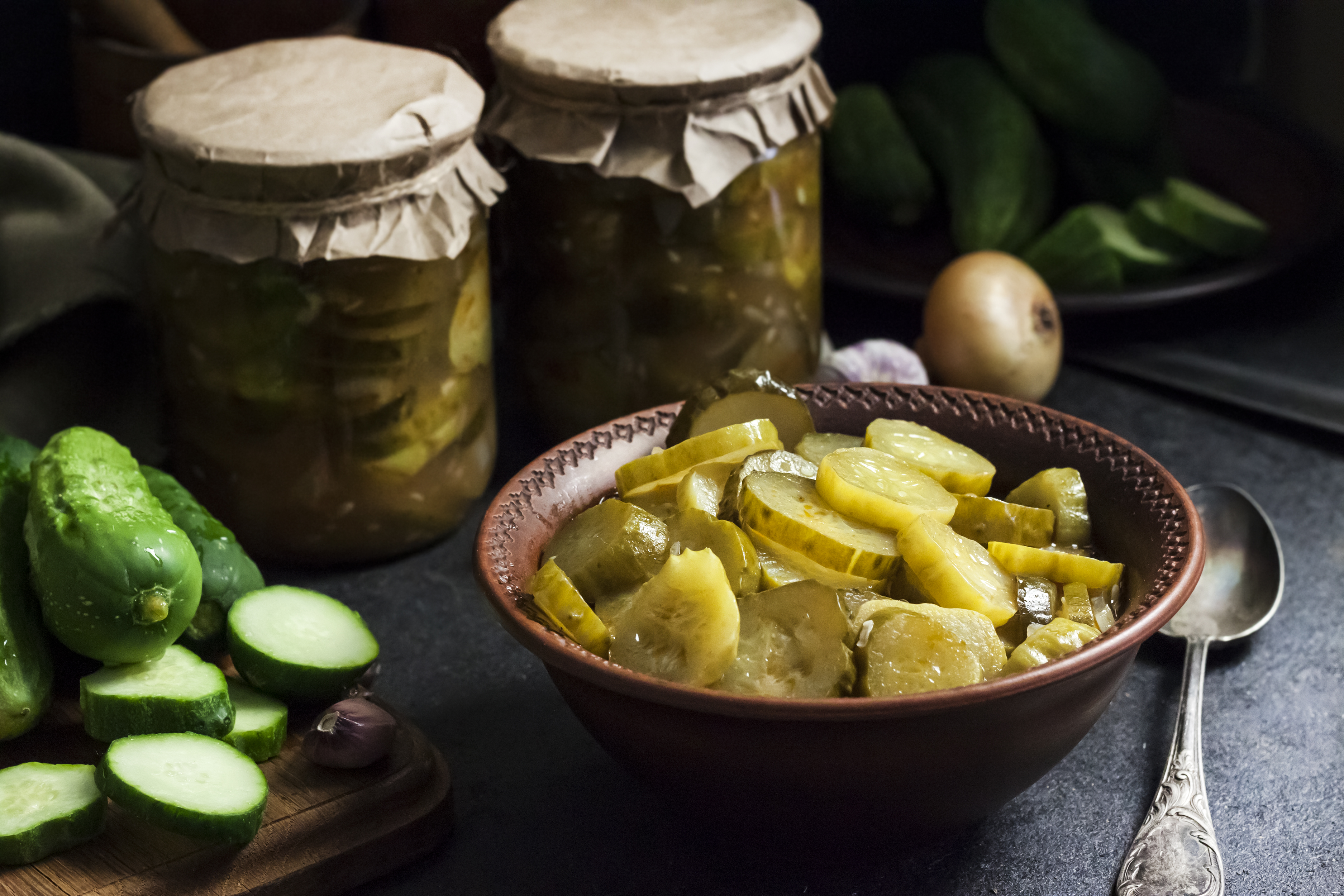 Pickled cucumber salad in a bowl and jars on black background
