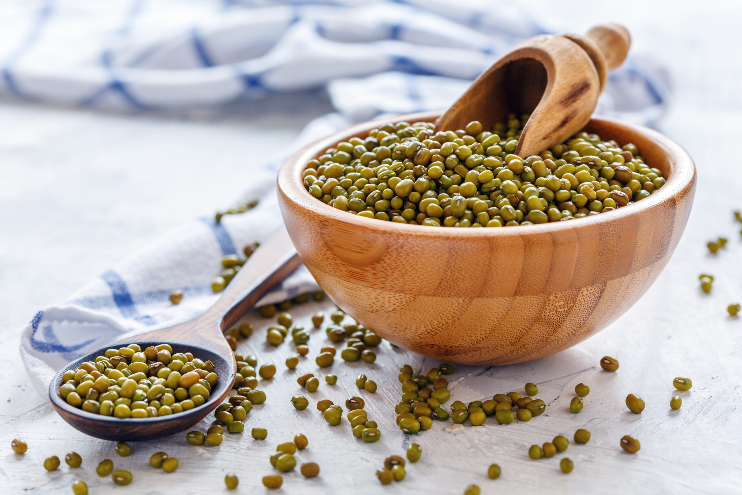 Mung beans in wooden bowl and spoon on white concrete table, selective focus.