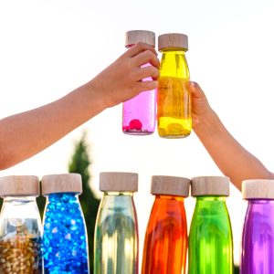 Happy kids toasting with toy bottles of vibrant colors with blue sky background.