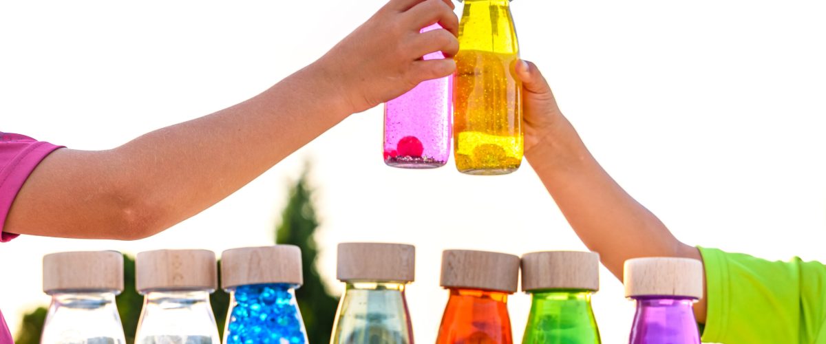 Happy kids toasting with toy bottles of vibrant colors with blue sky background.